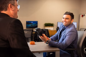 Mohsen Rakshan seated at a table holding EMG-based interface prototype, talking to Jonathan Beever, standing